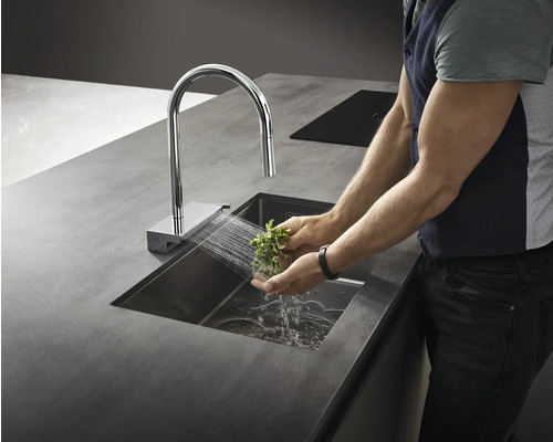 Person wäscht Kräuter in einer Spüle mit Wasserhahn in einer modernen Küche.