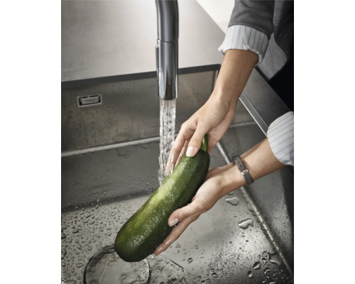 Person wäscht Zucchini in einer Edelstahlspüle unter einem Wasserhahn