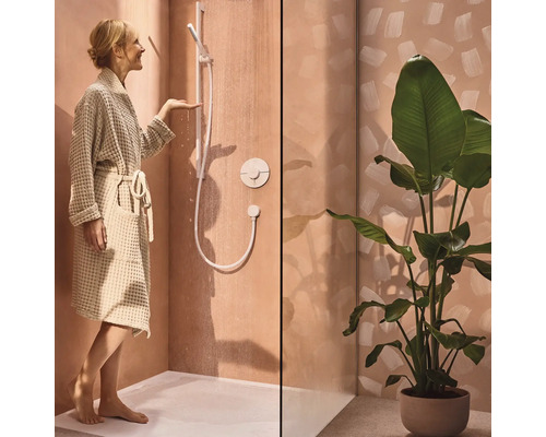 Frau mit Bademantel im Badezimmer mit Dusche und Topfpflanze.