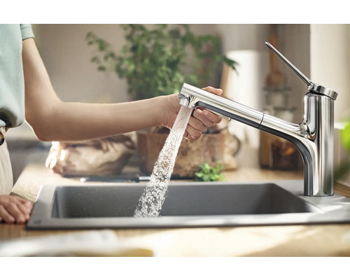 Eine Person benutzt eine Küchenarmatur mit Ausziehbrause über einem Spülbecken, aus der Wasser fließt.