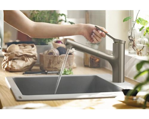 Eine Person bedient eine Küchenarmatur mit Wasserauslauf in einem modernen Küchenbereich.