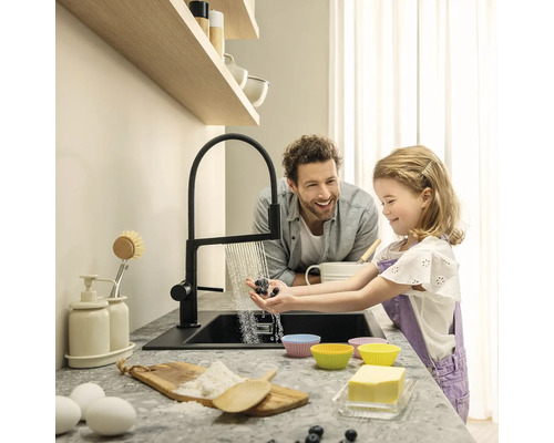 Szene einer Küche mit Vater und Tochter, die am Spülbecken Beeren waschen, mit einer modernen Armatur und Zutaten zum Backen auf der Arbeitsfläche.