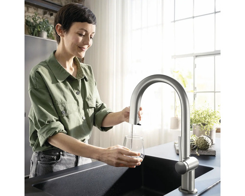 Frau füllt Wasser mit einer Küchenarmatur in ein Glas