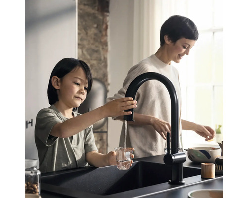 Kind füllt Wasser aus einem schwarzen Küchenarmatur in ein Glas