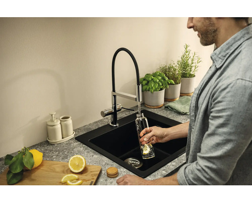 Schwarzes Spülbecken mit Wasserhahn, Kräutern und Zitrone in der Küche