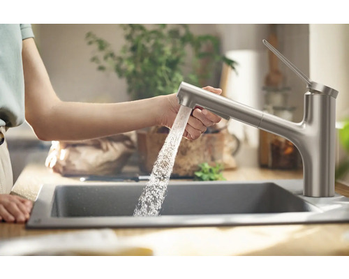 Frau bedient Küchenarmatur über Spüle