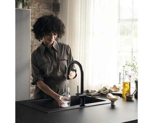 Eine Frau füllt eine Glasflasche mit einem schwarzen Wasserhahn in einer modernen Küche.