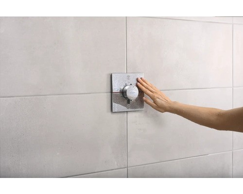Eine Hand betätigt einen Duschthermostat an einer gefliesten Wand