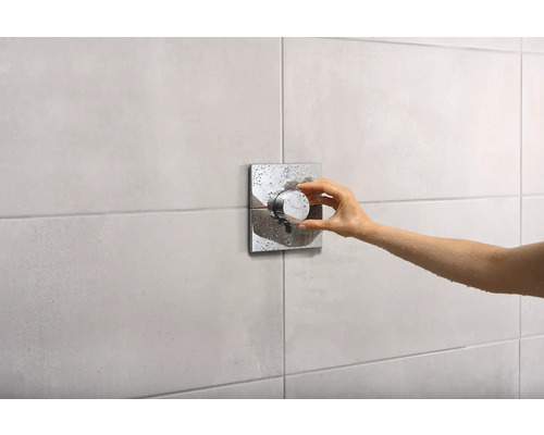 Eine Hand bedient einen Duschmischer mit quadratischer Rosette in einem Badezimmer.