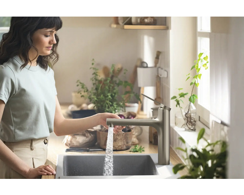 Frau benutzt Küchenarmatur mit Wasserhahn
