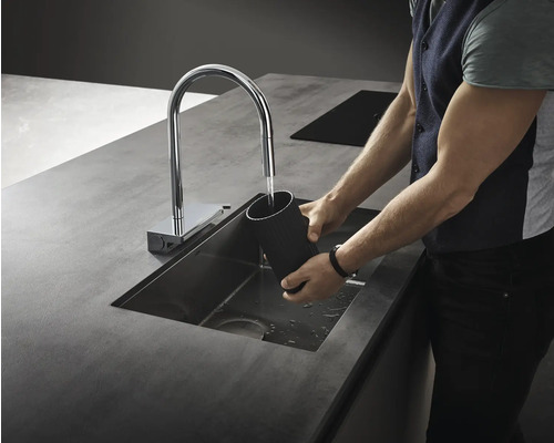 Eine Person wäscht ein Gefäß in einem Spülbecken mit Wasserhahn in einer Küche.