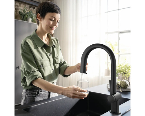 Frau füllt Wasser in ein Glas unter einem schwarzen Wasserhahn in einer Küche