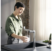 Frau füllt Glas mit Wasser am Spültisch mit Armatur