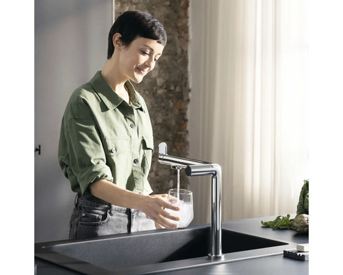 Frau füllt Glas mit Wasser am Spültisch mit Armatur