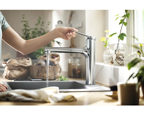 Eine Person bedient eine Küchenarmatur mit ausziehbarer Brause in einer hellen Küche.