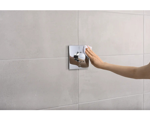 Eine Hand reinigt einen verchromten Duschthermostat an der Wand.