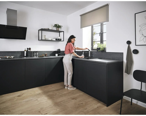 Moderne Küche mit schwarzen Schränken, Spüle und Armatur, Dunstabzugshaube, Regal und einer Frau, die ein Glas Wasser füllt.
