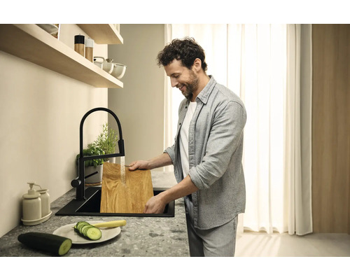 Mann wäscht ein Holzbrett in einer schwarzen Küchenspüle unter einem schwarzen Wasserhahn.