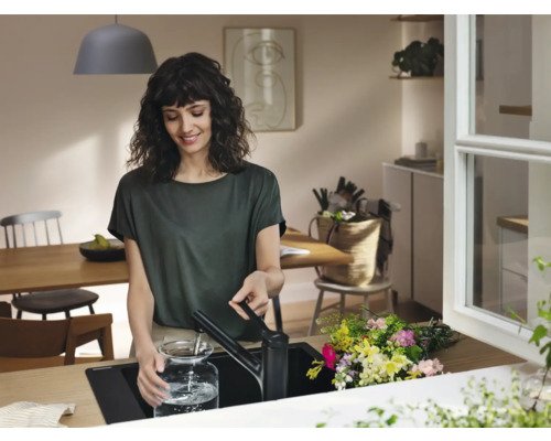 Frau befüllt Glasgefäß mit Wasserhahn in moderner Küche