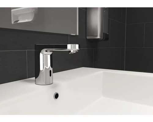 Berührungsloser Wasserhahn auf einem weißen Waschbecken mit grauen Fliesen im Hintergrund