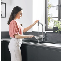 Frau spült Lebensmittel im Küchensieb unter einem Wasserhahn in einer modernen Küche.