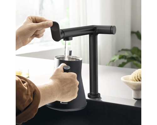 Eine Person befüllt einen Wasserkocher mit einem Wasserhahn in einer Küche.