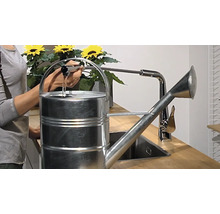 Eine Person befüllt eine Metallgießkanne an einem Wasserhahn.