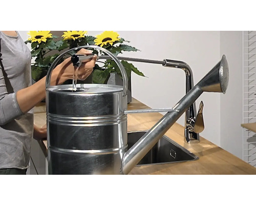 Eine Person befüllt eine Metallgießkanne an einem Wasserhahn.