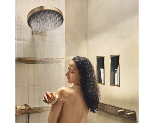 Frau unter einer runden Regendusche in einem Badezimmer mit eingebauten Ablagen und Messingdetails