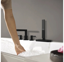 Frau lässt Wasser in eine Badewanne mit schwarzer Armatur einlaufen.