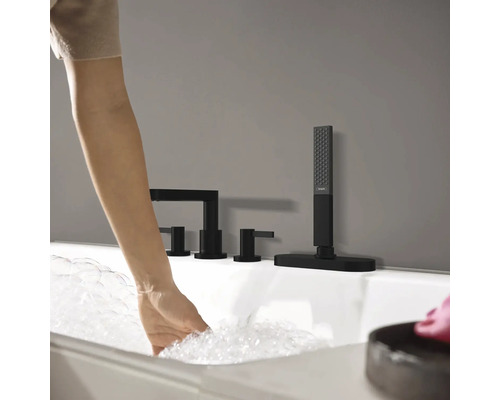 Frau lässt Wasser in eine Badewanne mit schwarzer Armatur einlaufen.