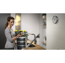 Frau befüllt eine silberfarbene Gießkanne am Wasserhahn in einer Küche.