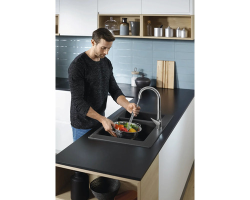 Ein Mann wäscht Gemüse in einem Küchenspülbecken mit einer Armatur.