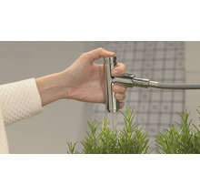 Eine Hand betätigt einen Wasserhahn aus Metall, aus dem Wasser über eine Pflanze fließt.