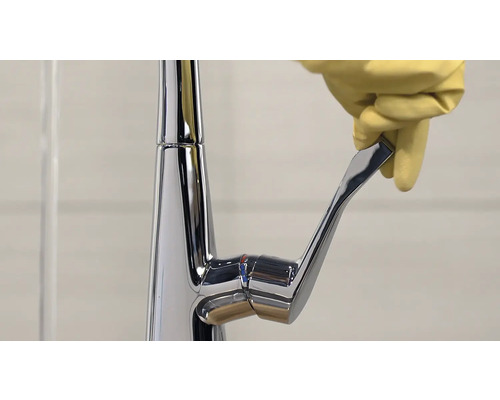 Armatur aus Chrom mit Hand und gelbem Handschuh, der den Hebel bedient