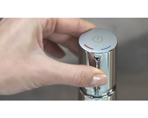 Eine Hand betätigt einen verchromten Wasserhahn mit Temperaturregelung