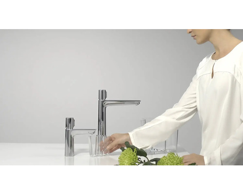 Zwei glänzende Waschtischarmaturen auf einem Waschtisch mit Glas und Frau