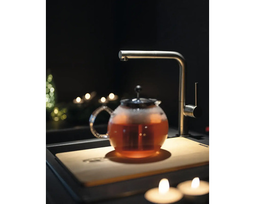 Teekanne mit Tee, Wasserhahn und Schneidebrett in einer dunklen Küchenszene.