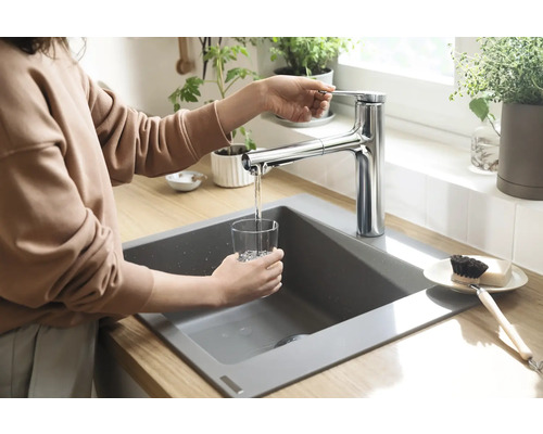 Frau füllt ein Glas Wasser an einem Spültisch mit einer Armatur.