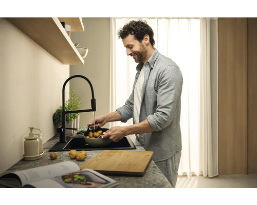 Mann wäscht Kartoffeln in einer modernen Küche mit schwarzem Spülbecken und Armatur.