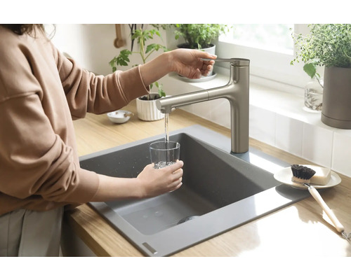 Eine Person füllt ein Glas Wasser an einem Küchenspültisch mit Armatur
