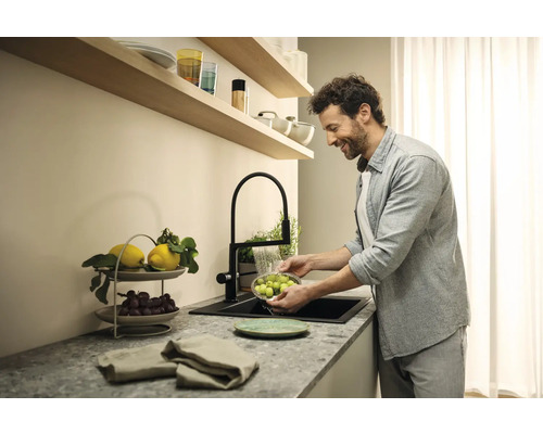 Mann wäscht Obst in einer Küchenspüle mit einem schwarzen Wasserhahn
