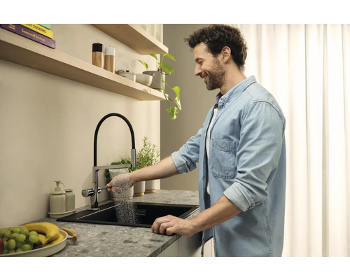 Ein Mann benutzt eine Küchenarmatur mit Brausefunktion an einem modernen Spültisch