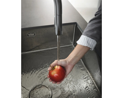 Eine Person wäscht einen Apfel in einem Edelstahlspülbecken unter einem Wasserhahn.