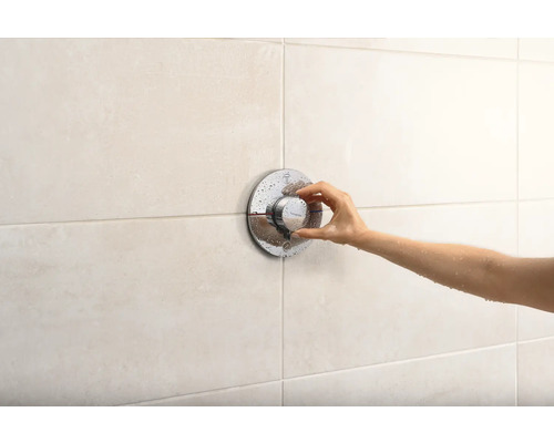 Eine Hand bedient einen runden Duschthermostat an einer gefliesten Wand