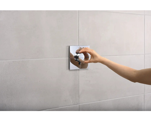 Hand betätigt einen quadratischen Thermostat an einer gefliesten Wand