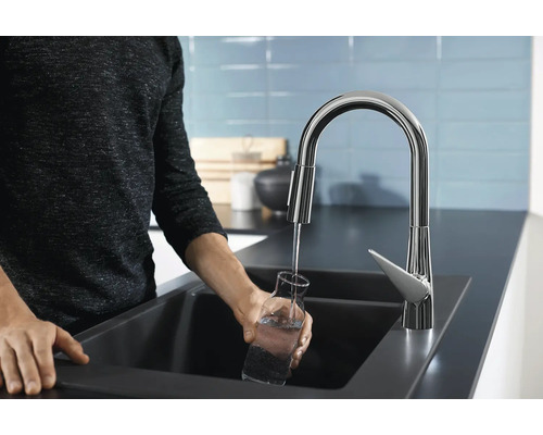 Eine Person füllt ein Glas Wasser an einem Spültisch mit einer Armatur.
