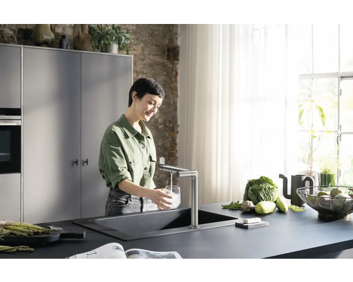 Frau befüllt Glas mit Wasser an Küchenspüle mit Armatur in moderner Küche