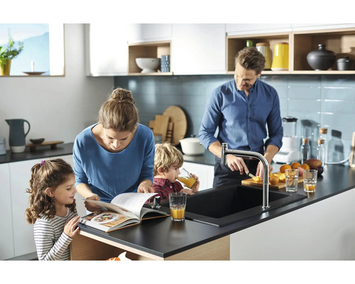 Familie bereitet in einer hellen Küche mit Küchenarmatur und Spüle Speisen zu.