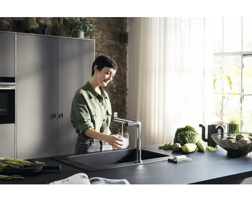 Frau füllt Wasser in ein Glas am Spültisch mit Armatur in einer modernen Küche